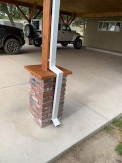 Custom downspout wrapped around a brick patio pillar